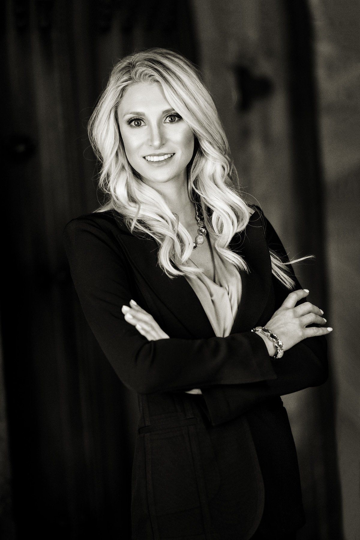 A black and white photo of a woman in a suit holding a glass of wine.