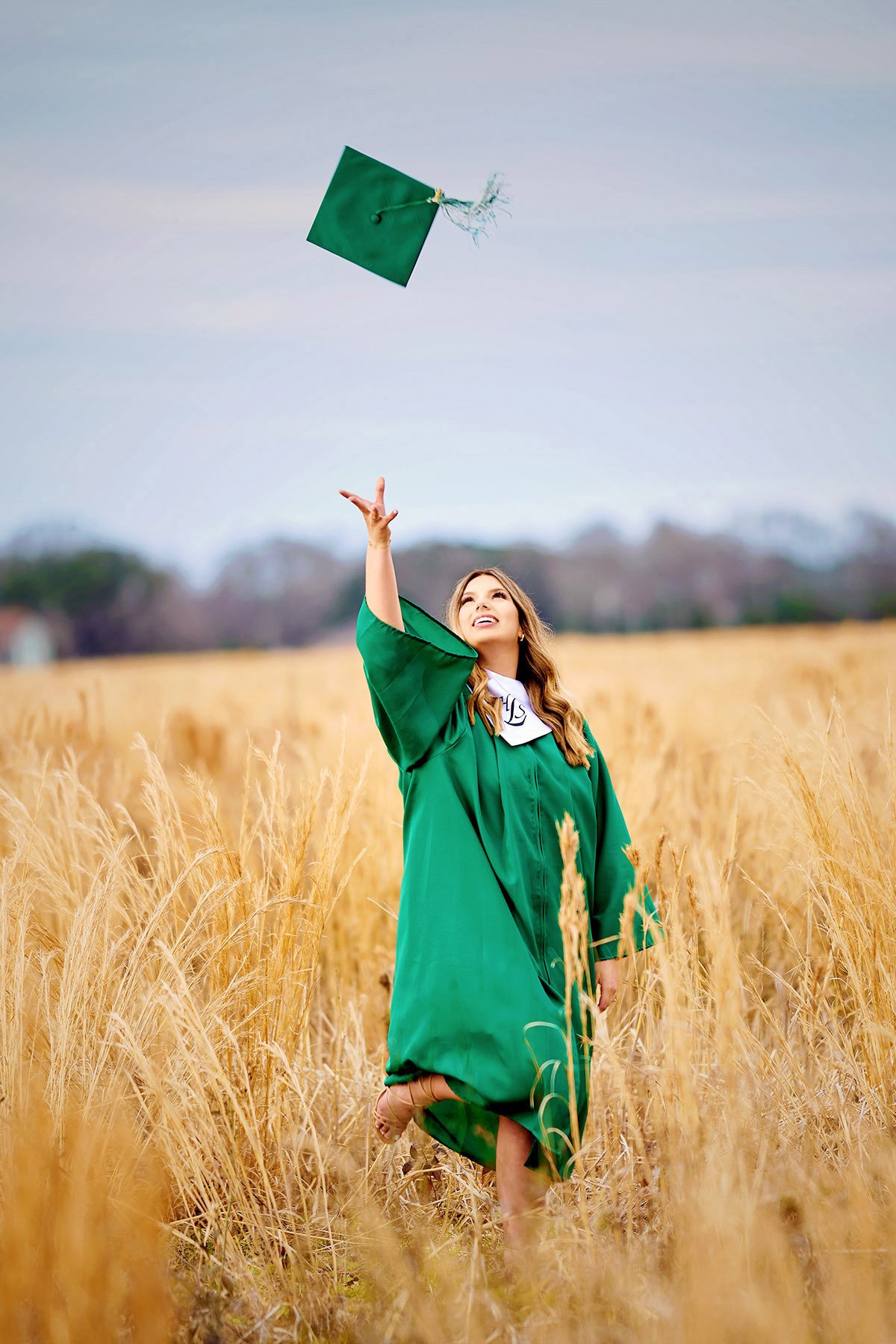 A woman in a green gown is throwing her graduation cap in the air.