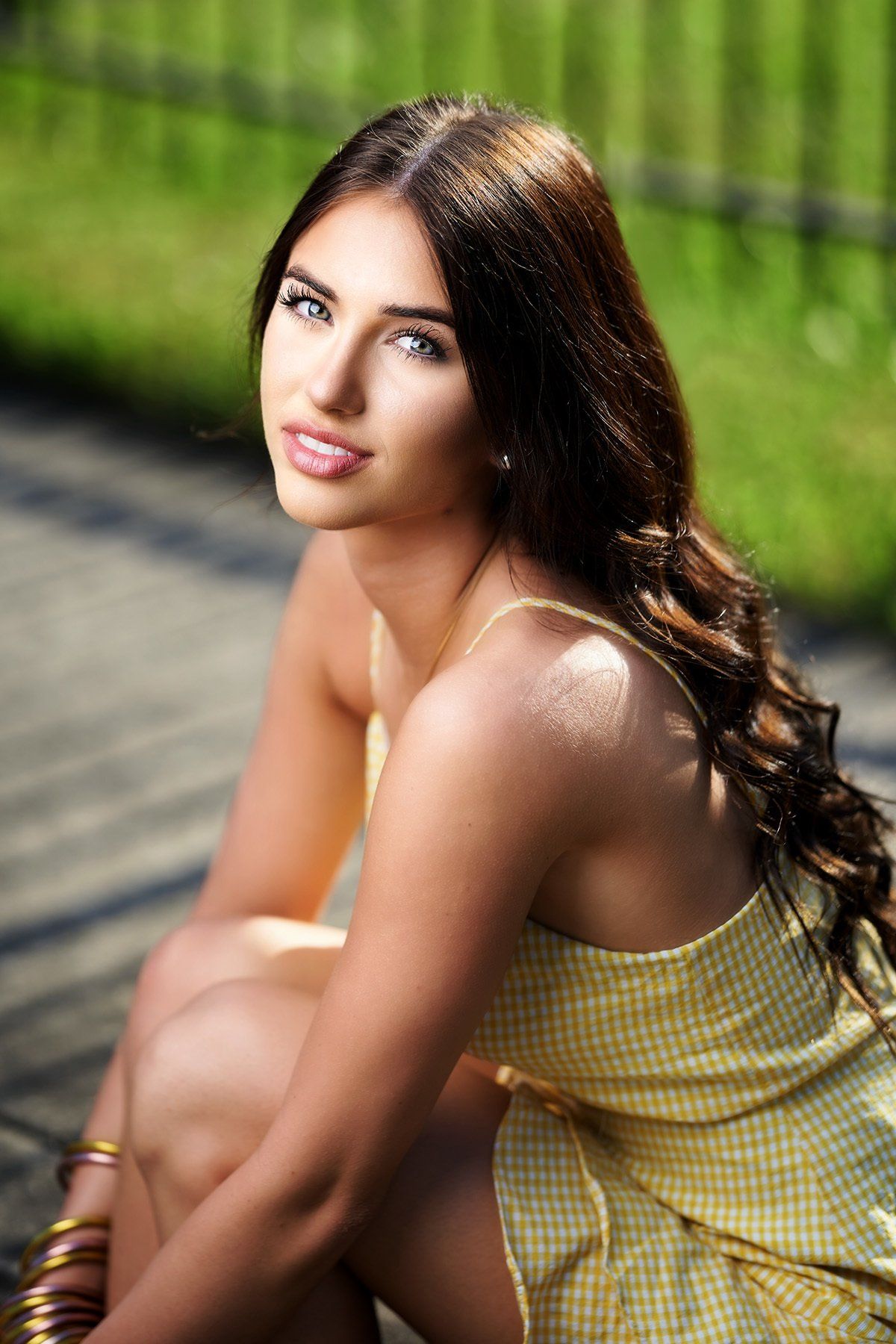 A woman in a yellow dress is sitting on the ground looking at the camera.