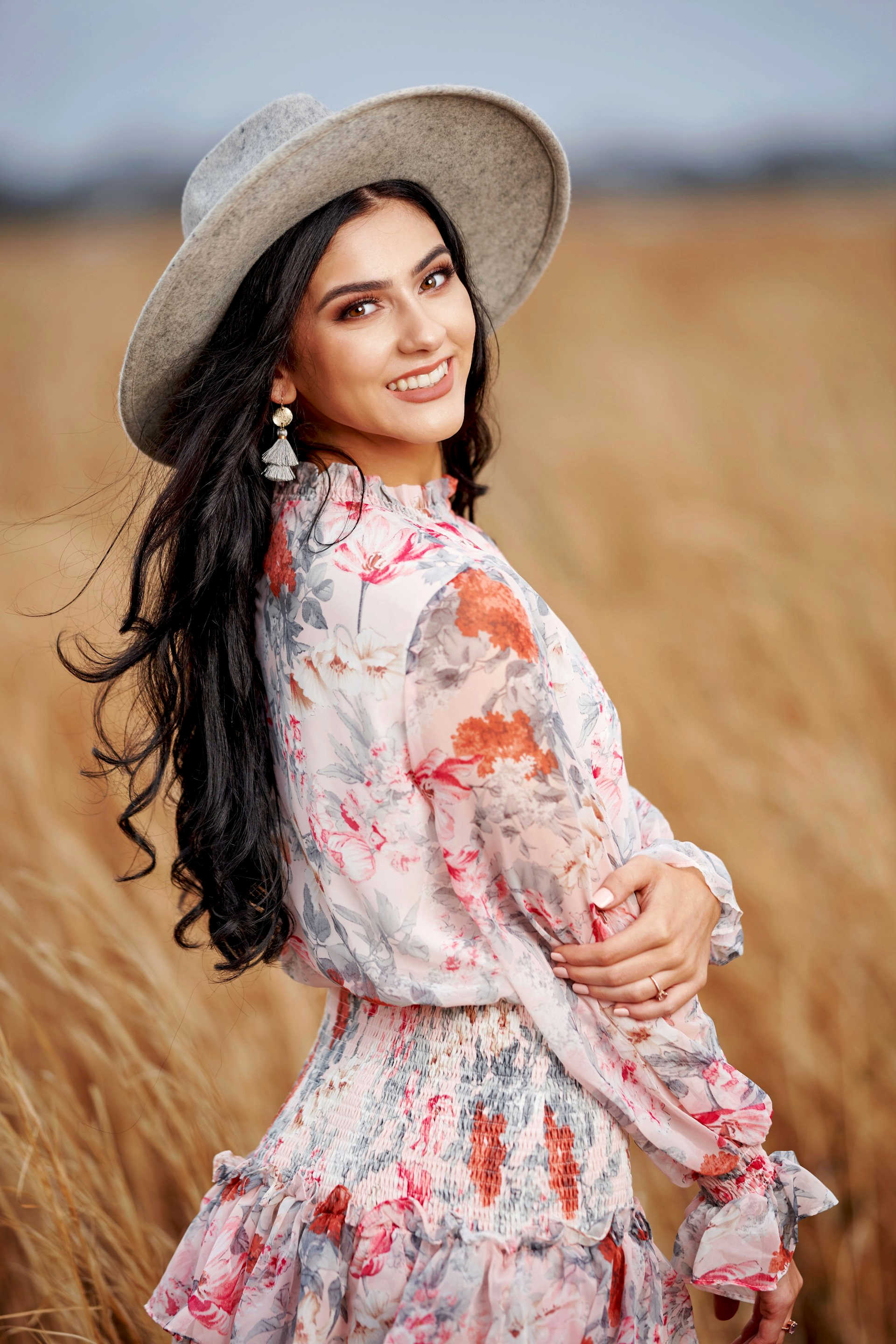 A woman in a floral dress and hat is standing in a field of wheat.
