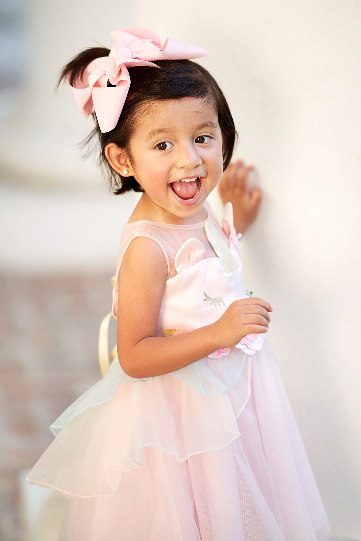 A little girl is wearing a pink dress and a pink bow in her hair.