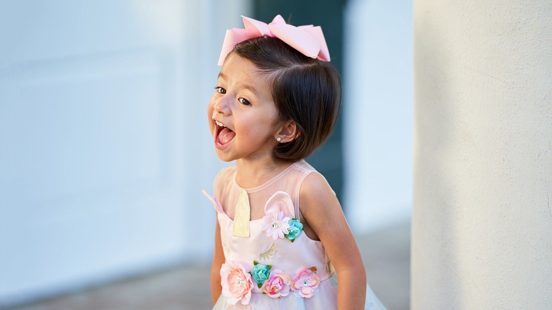 A little girl is wearing a pink dress and a pink bow in her hair.