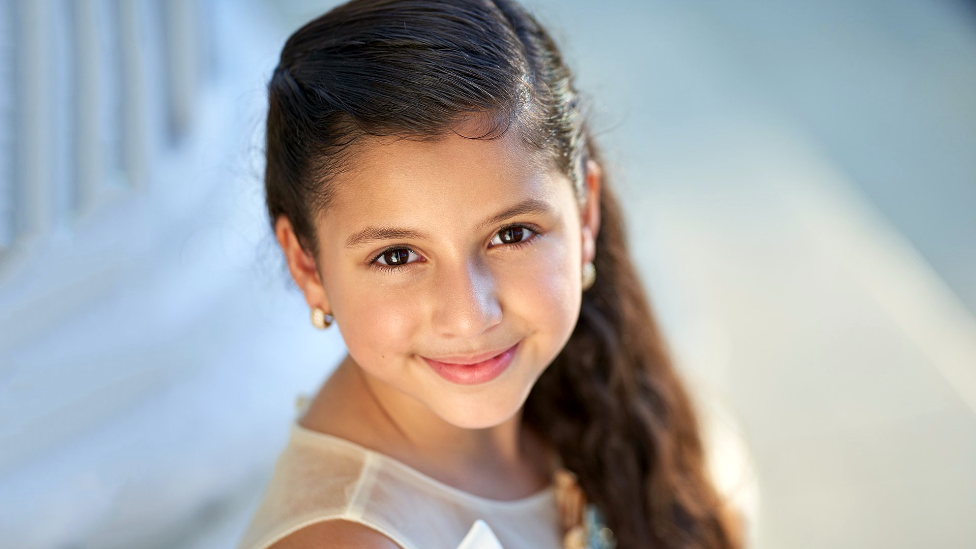 A young girl in a white dress is smiling for the camera.