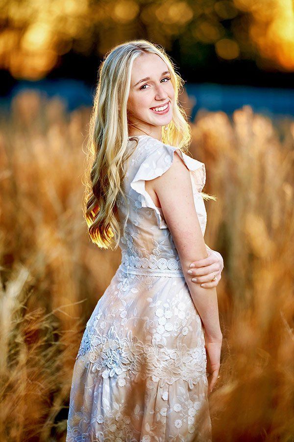 A woman in a white dress is standing in a field of tall grass.