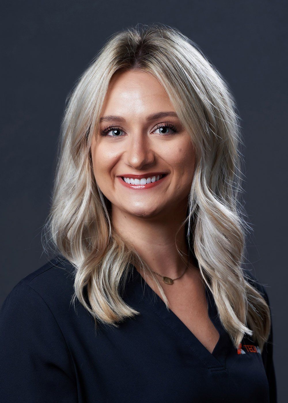 A woman with blonde hair is wearing a black shirt and smiling for the camera.