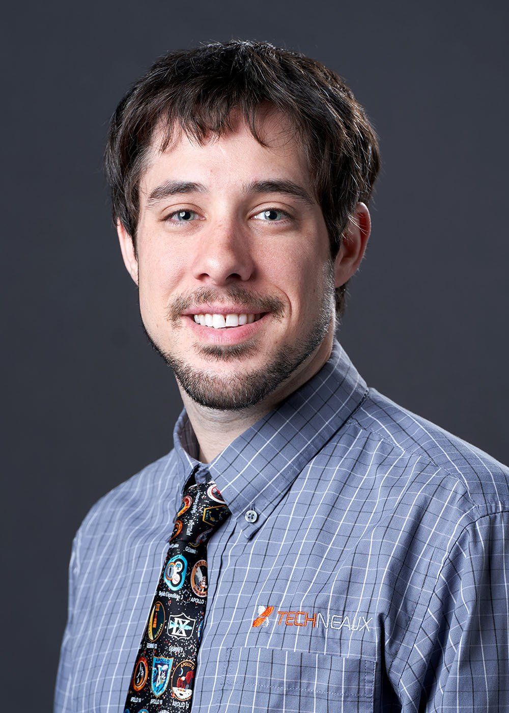 A man wearing a blue shirt and tie is smiling for the camera.