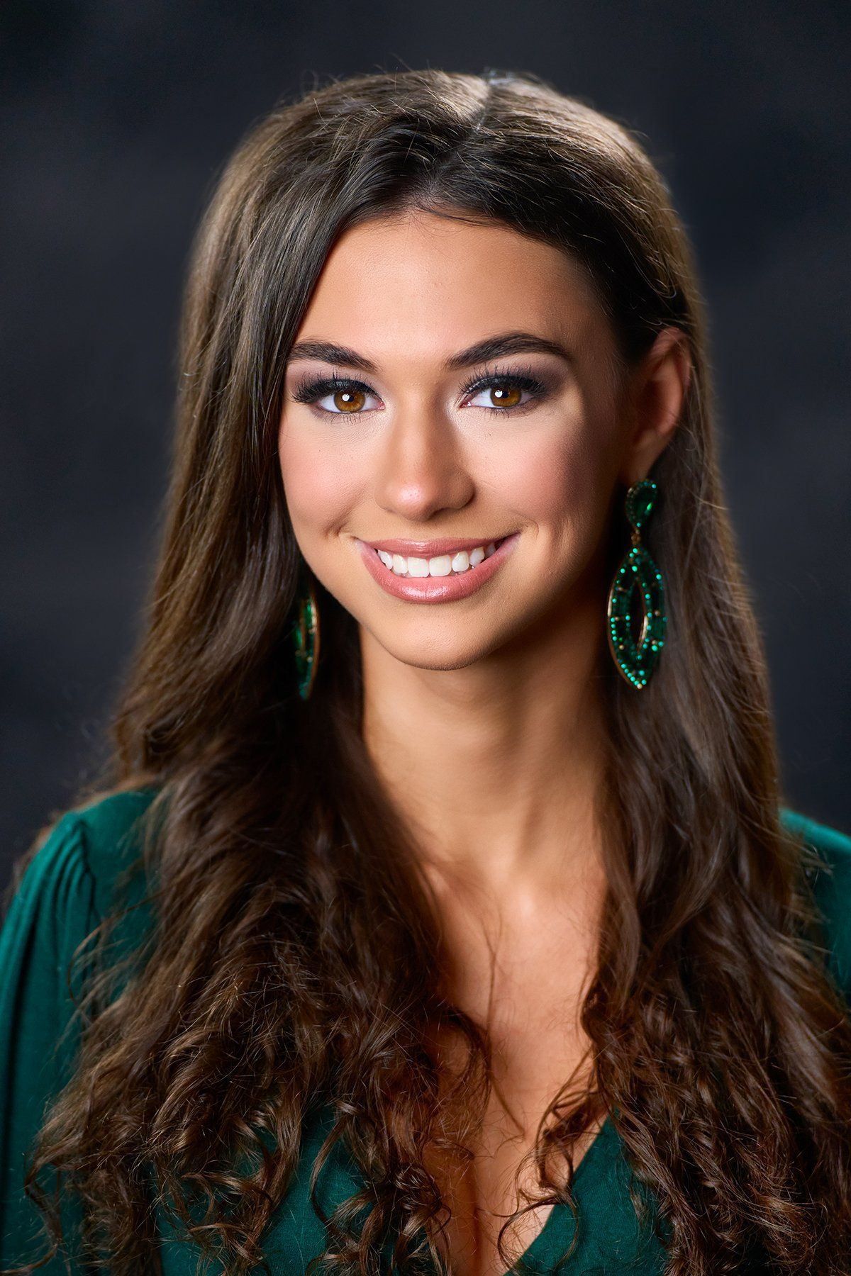 A woman with long hair and green earrings is smiling for the camera.
