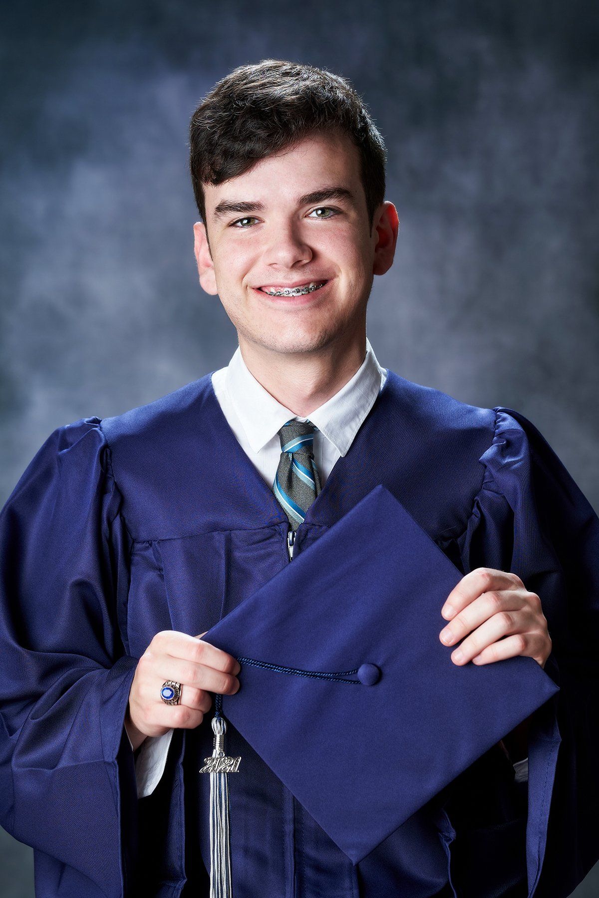 A young man in a graduation cap and gown is holding his cap.