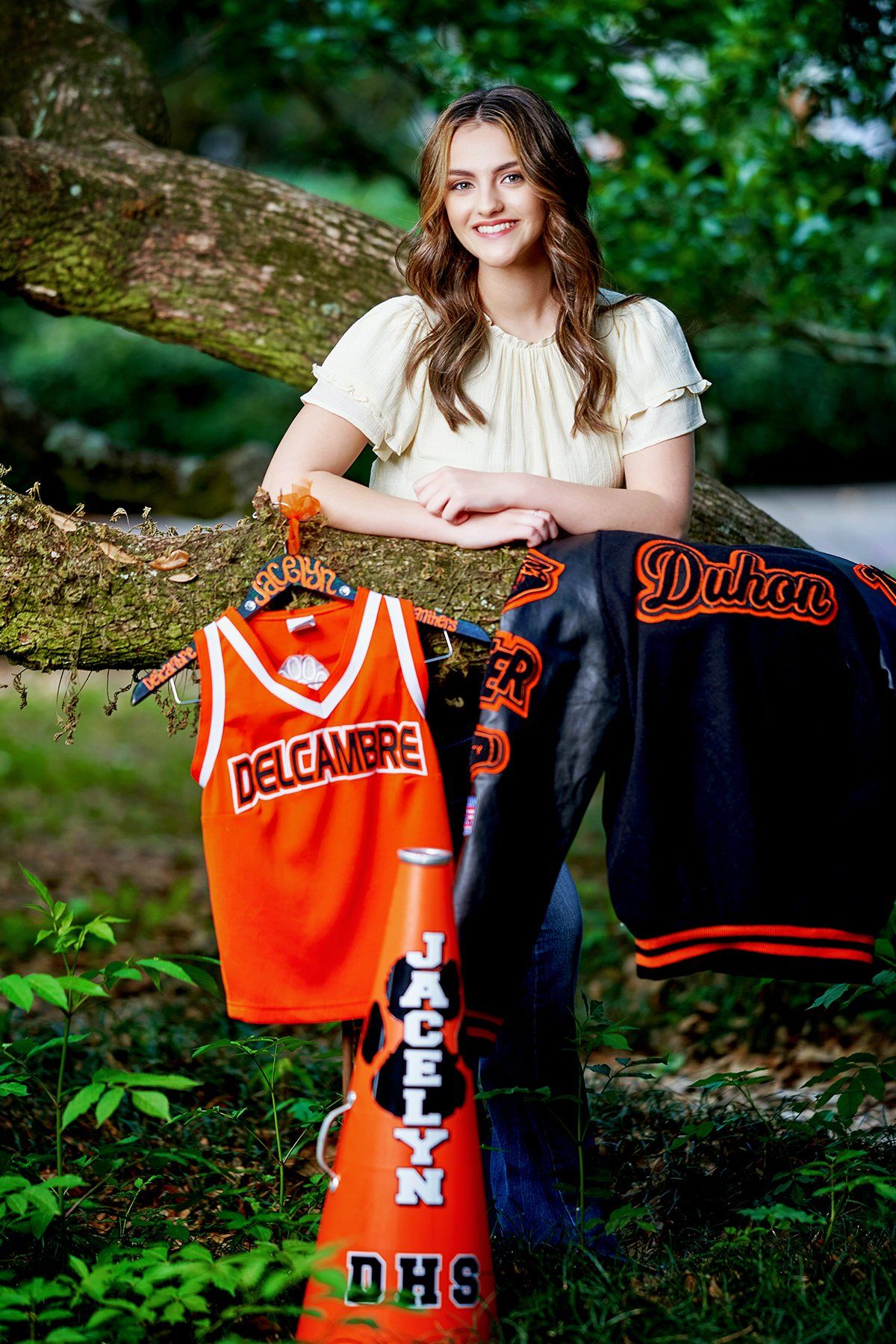 A woman is standing next to a tree holding a jersey and a cheerleader 's horn.