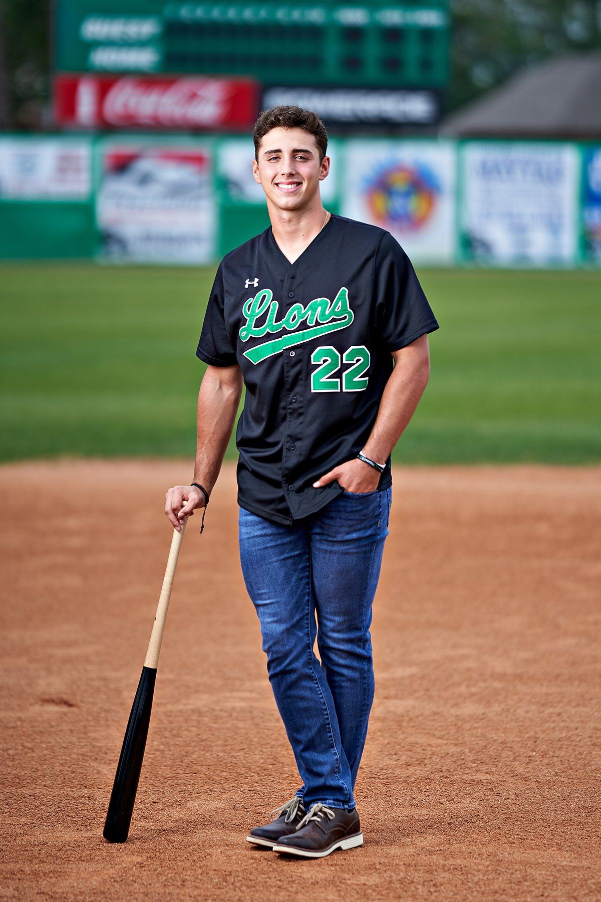 A young man is standing on a baseball field holding a bat.
