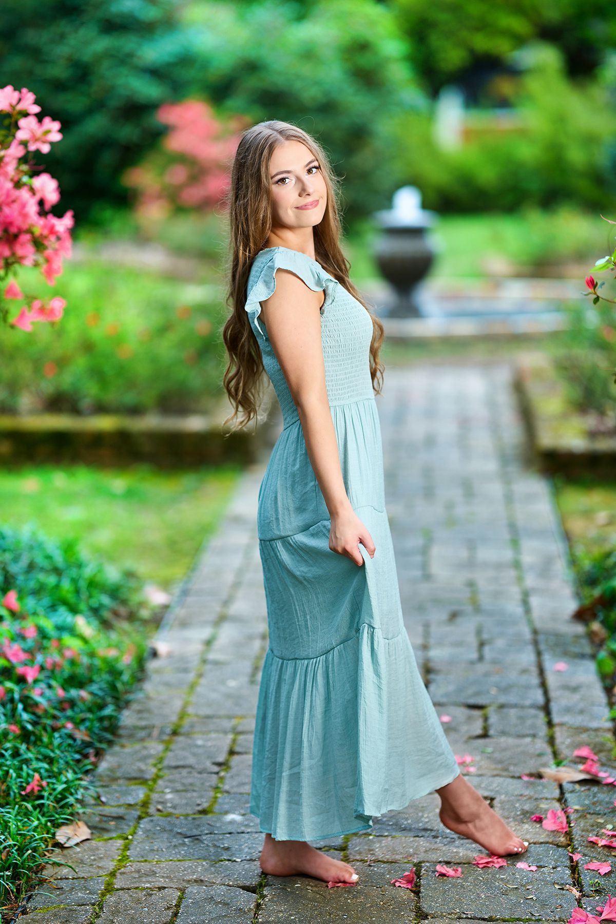 A woman in a blue dress is standing on a brick path in a garden.