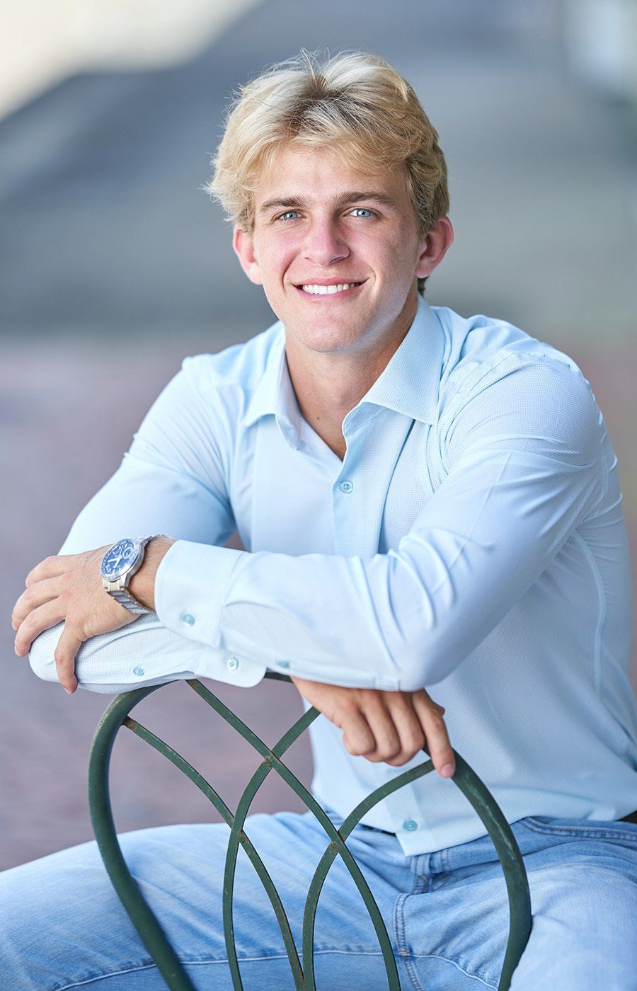 A young man is sitting on a chair with his arm resting on a railing.
