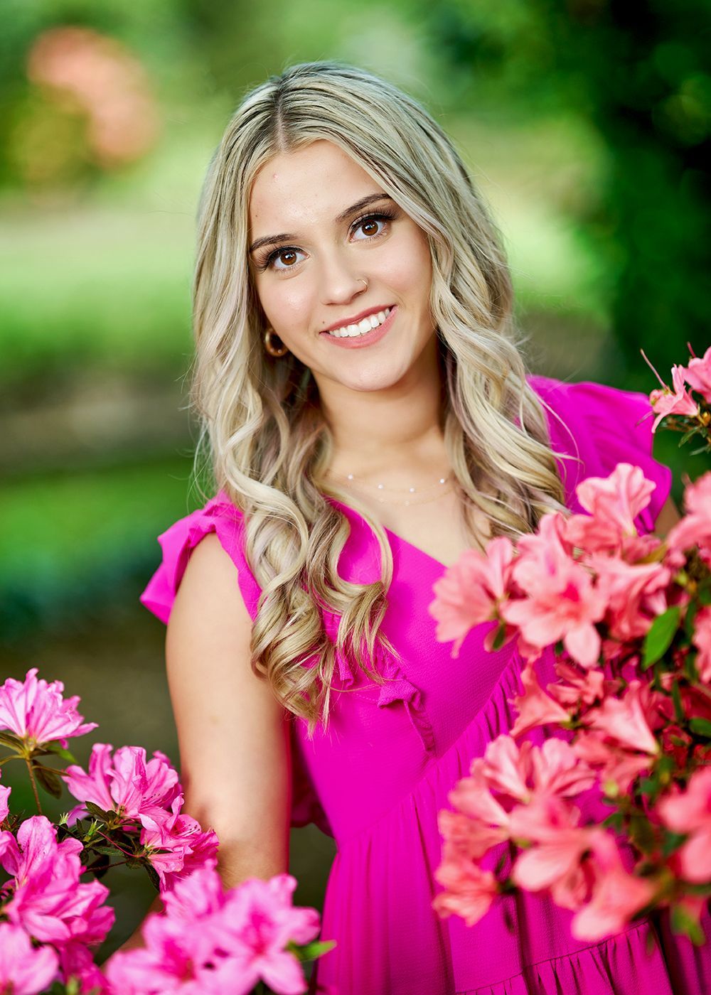 A woman in a pink dress is standing in front of a bush of pink flowers.