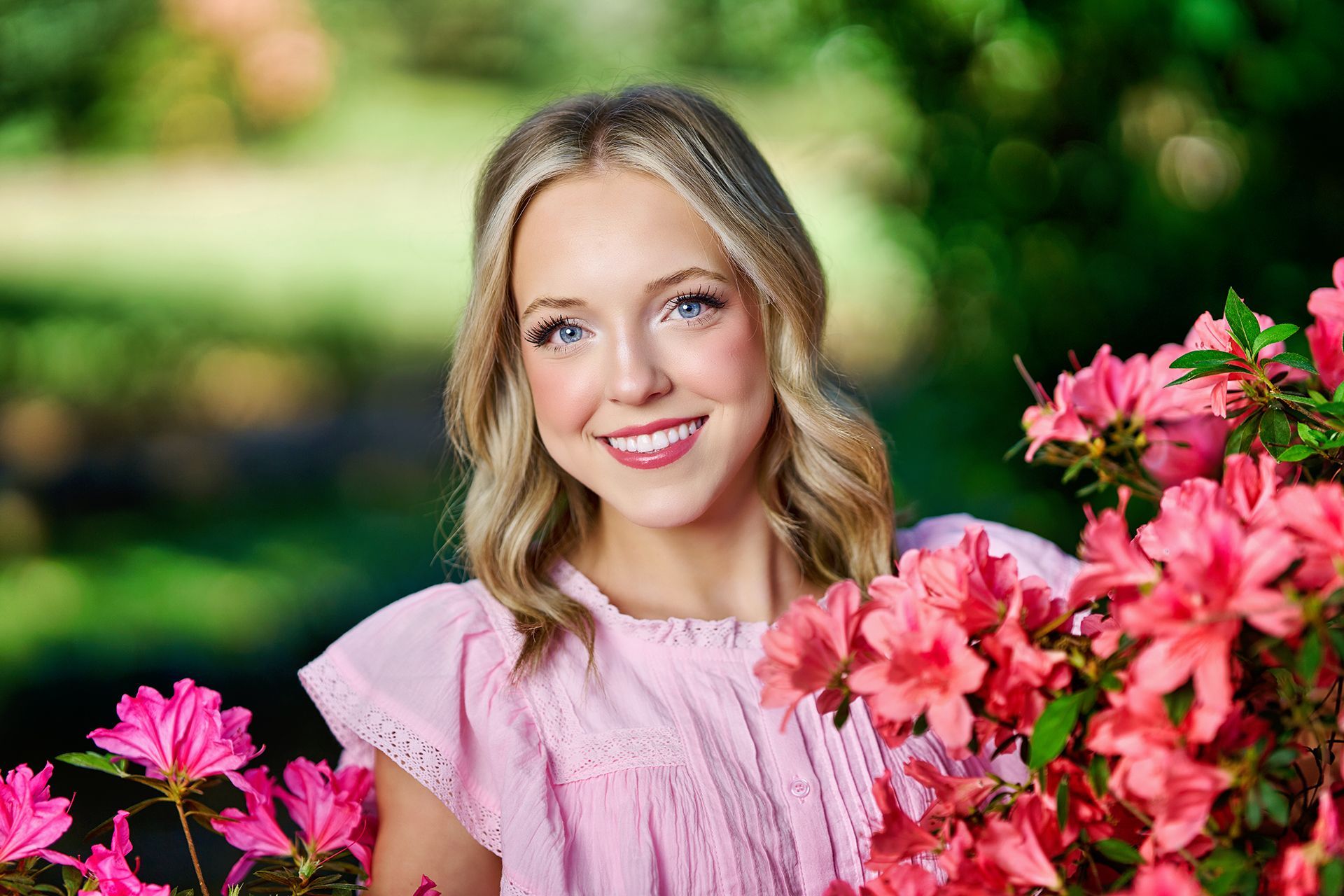 A woman in a pink dress is standing next to a bush of pink flowers.