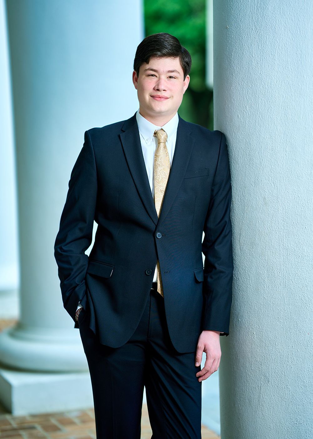A young man in a suit and tie is leaning against a pillar.