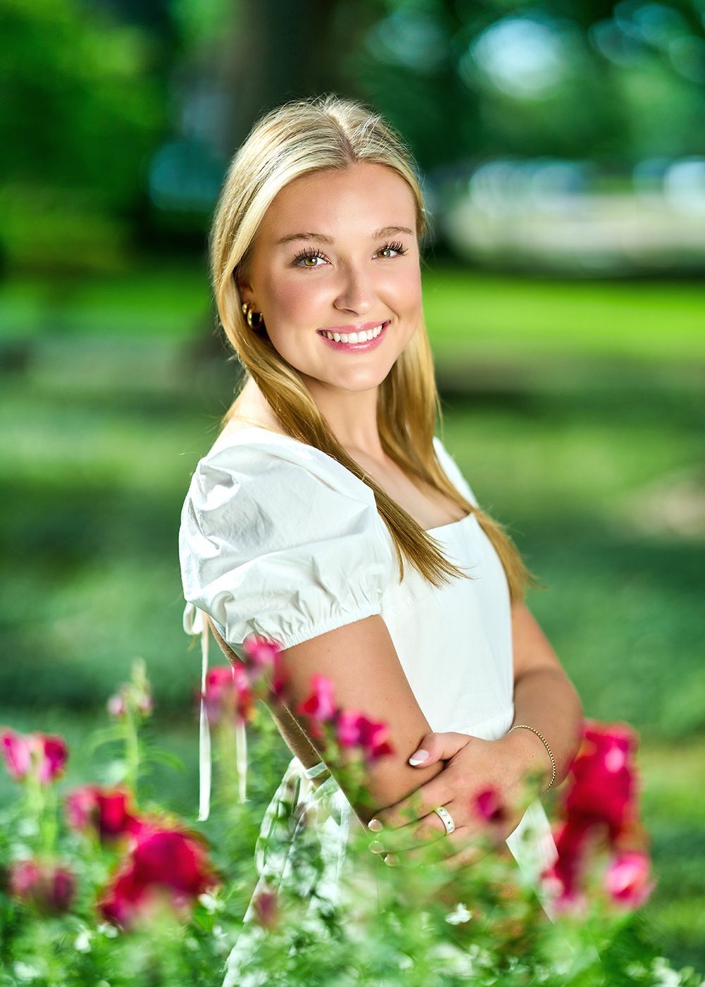 A young woman in a white dress is standing in a field of flowers.