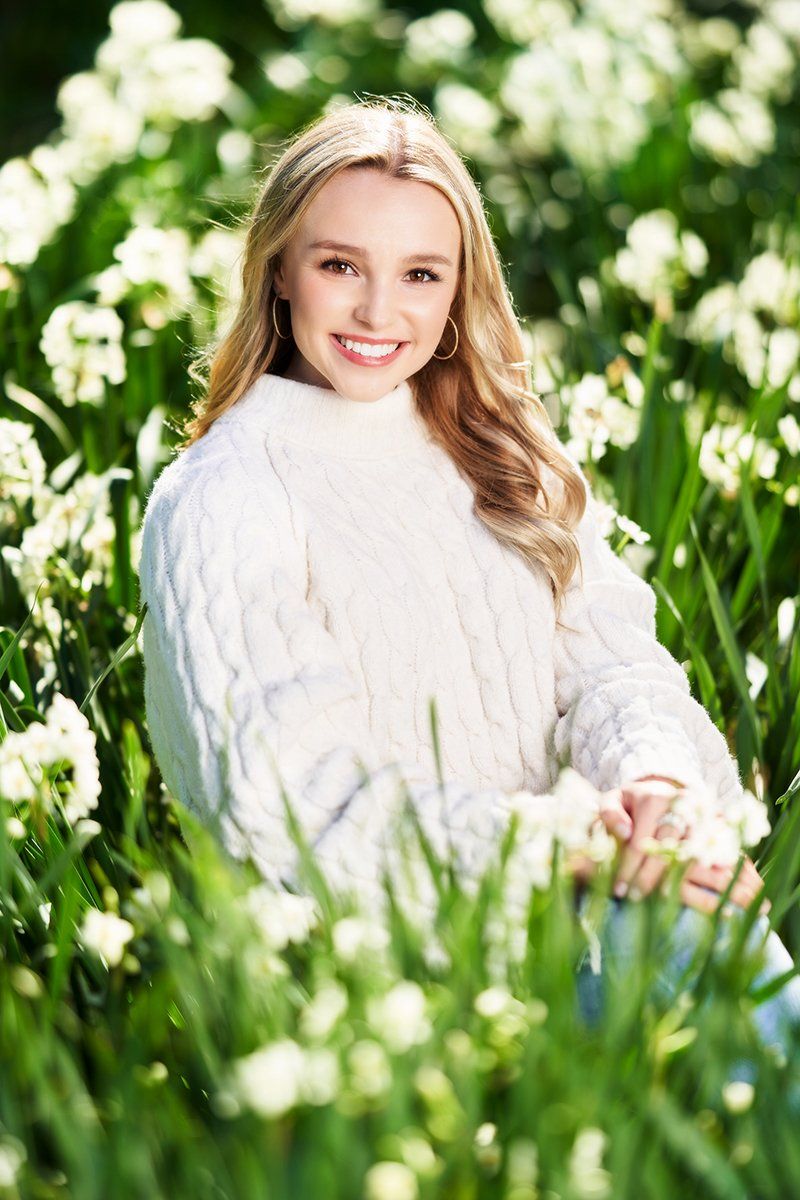 A young woman in a white sweater is sitting in a field of white flowers.