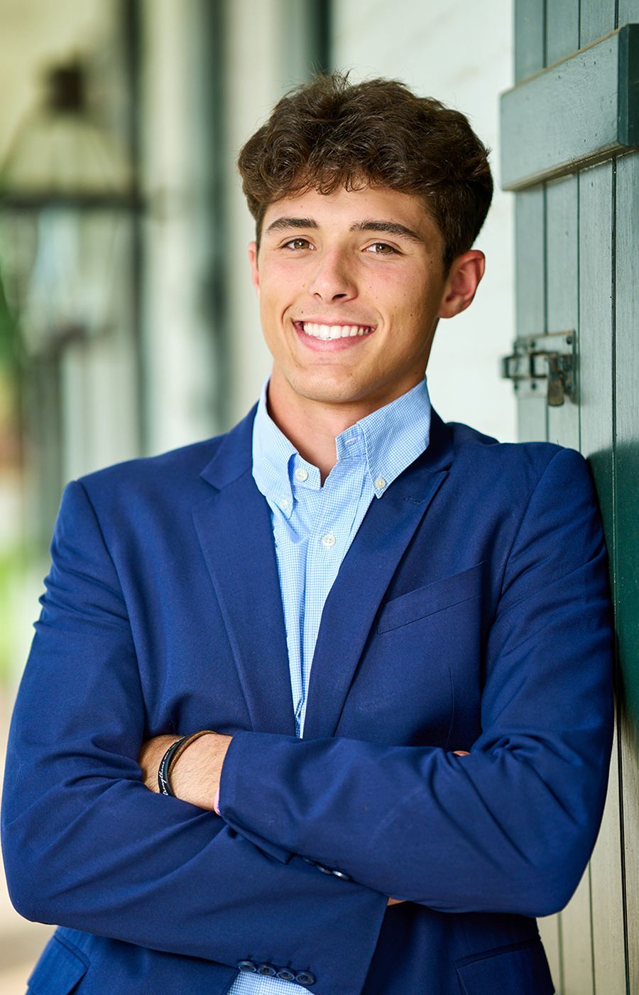 A young man in a blue suit is standing with his arms crossed and smiling.