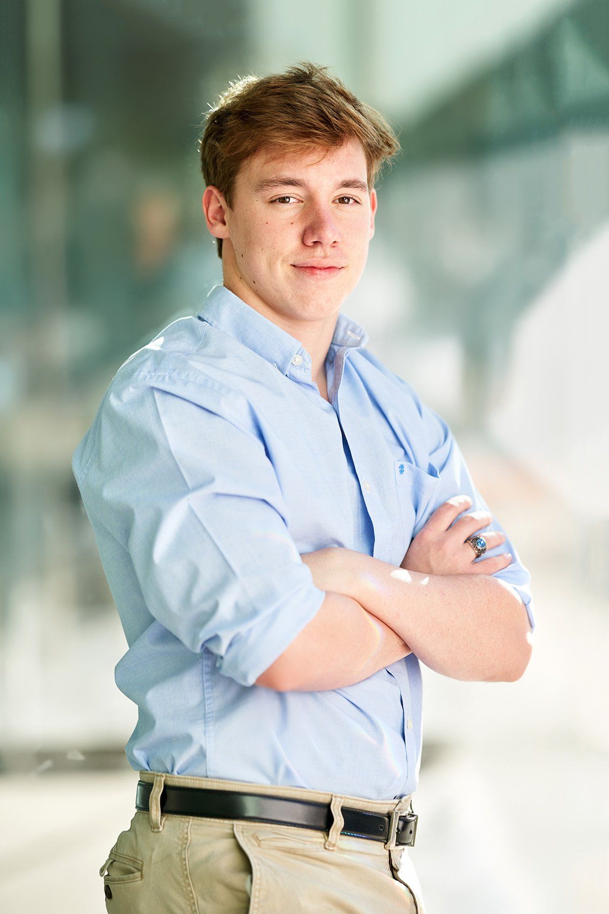 A young man in a blue shirt and khaki pants is standing with his arms crossed.