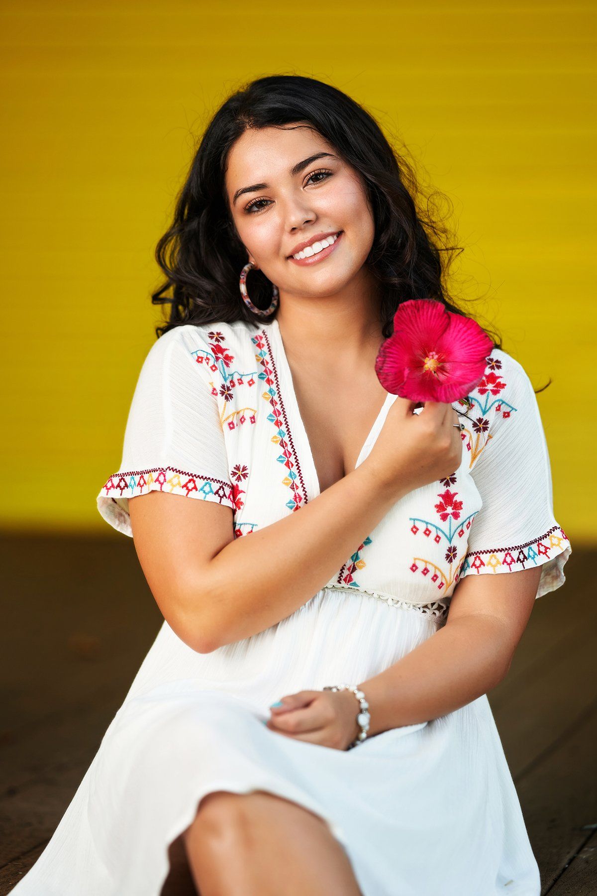 A woman in a white dress is holding a red flower.