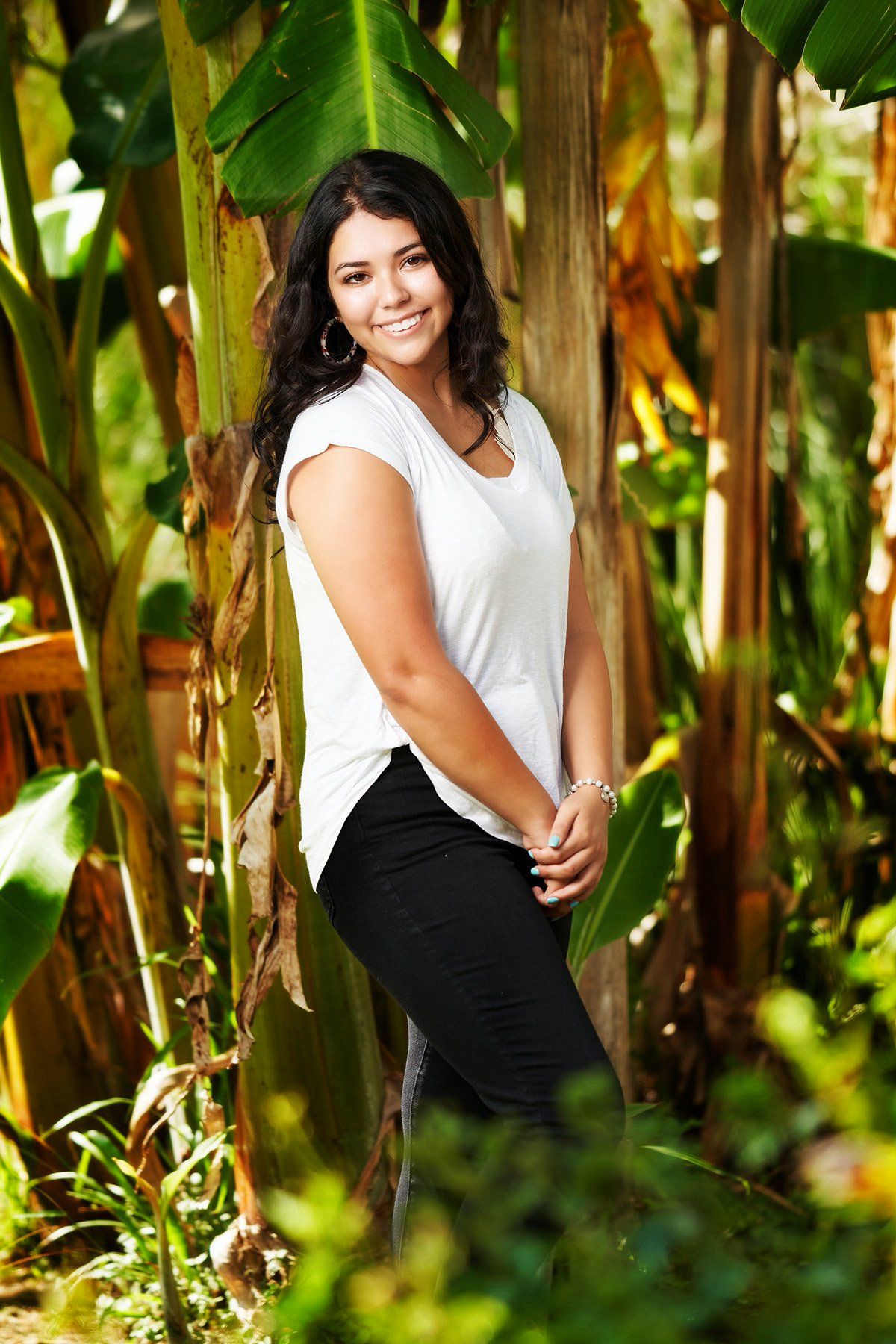 A young woman is standing next to a tree in the woods.