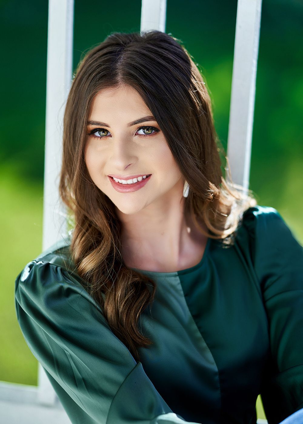 A woman in a green dress is smiling for the camera while sitting on a porch.