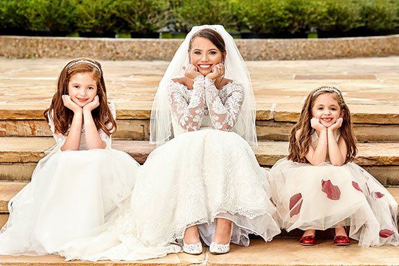 A bride and her two flower girls are posing for a picture.