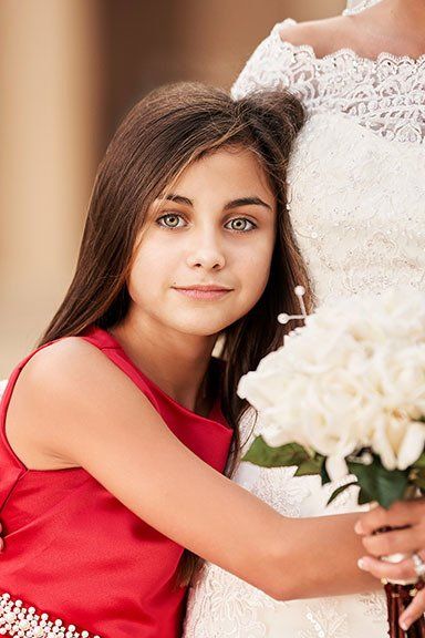 A little girl in a red dress is hugging a bride in a wedding dress.