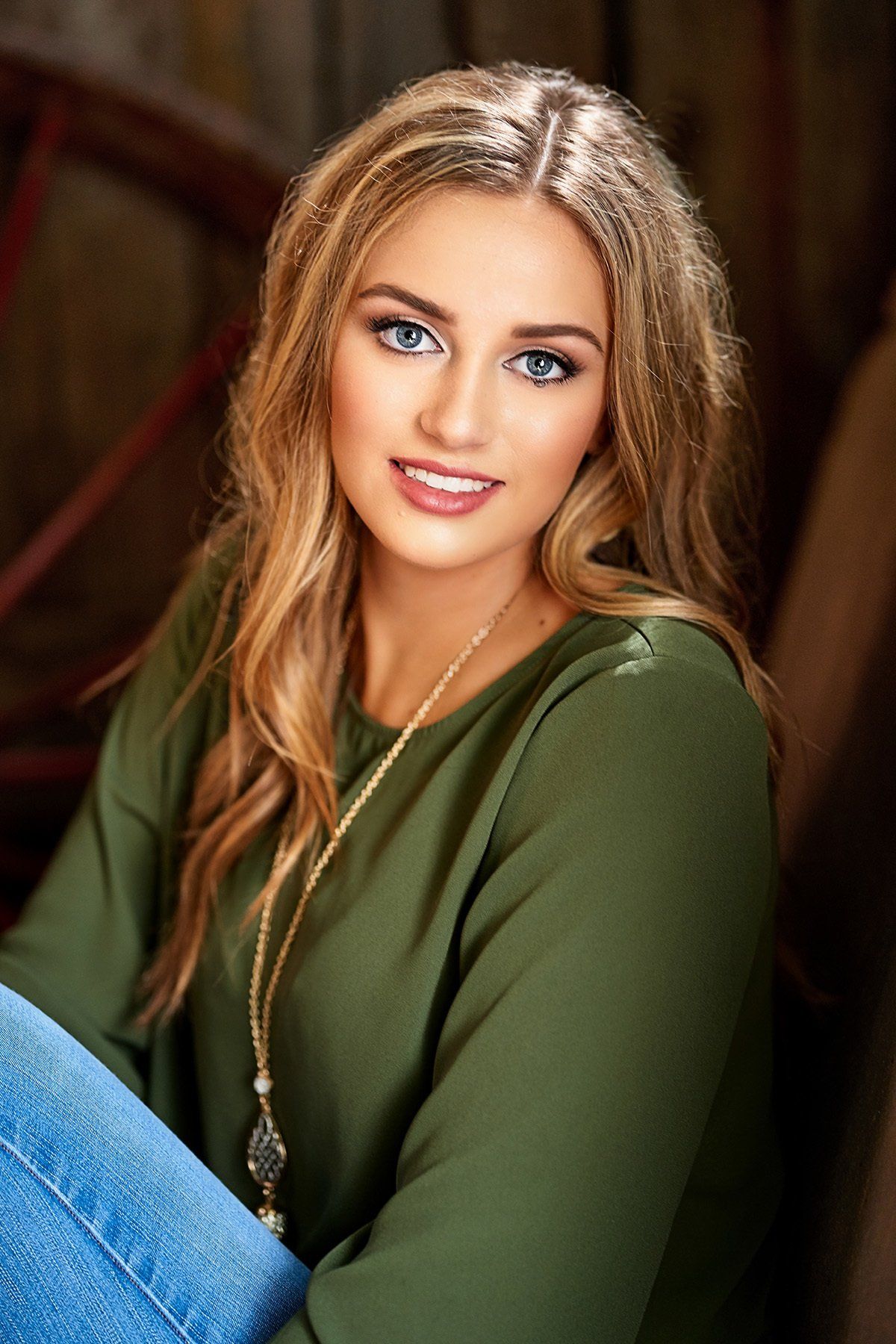 The woman is wearing a green shirt and blue jeans and is sitting down.