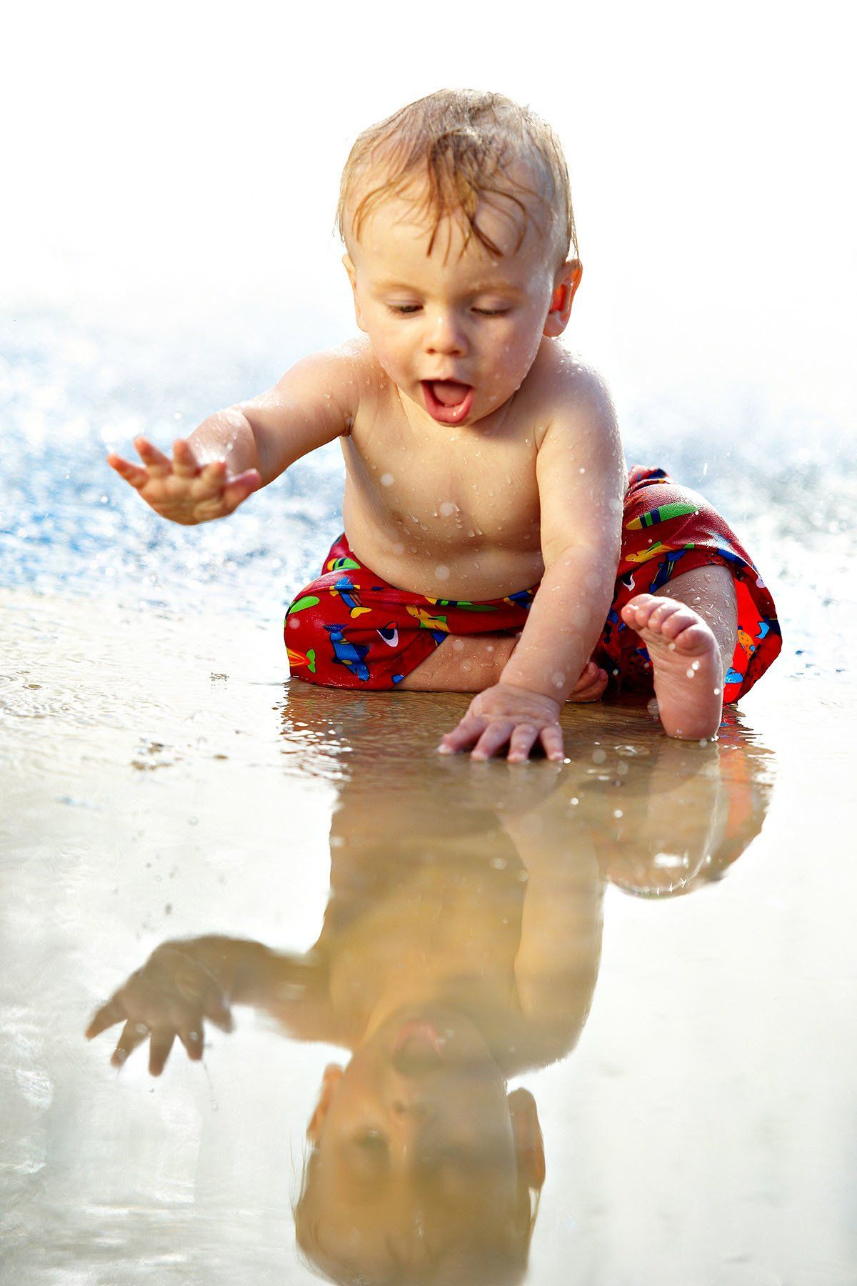 A baby is sitting in a puddle of water on the beach.