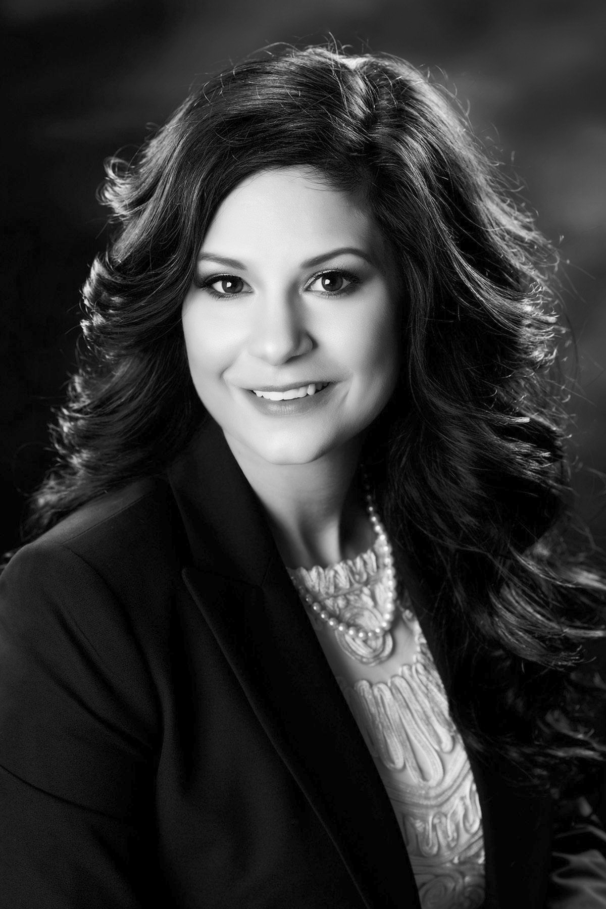 A black and white photo of a woman wearing a jacket and pearls.