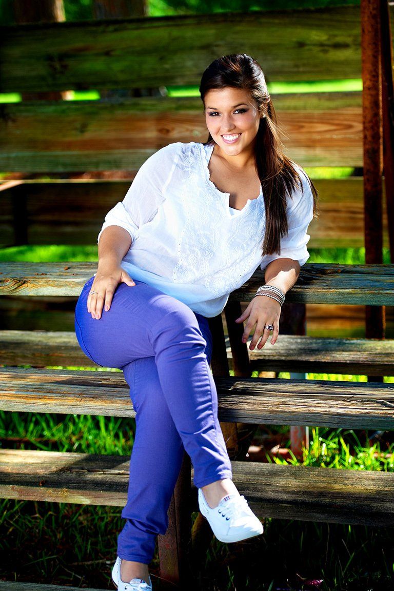 A woman in a white shirt and blue pants is sitting on a wooden bench.