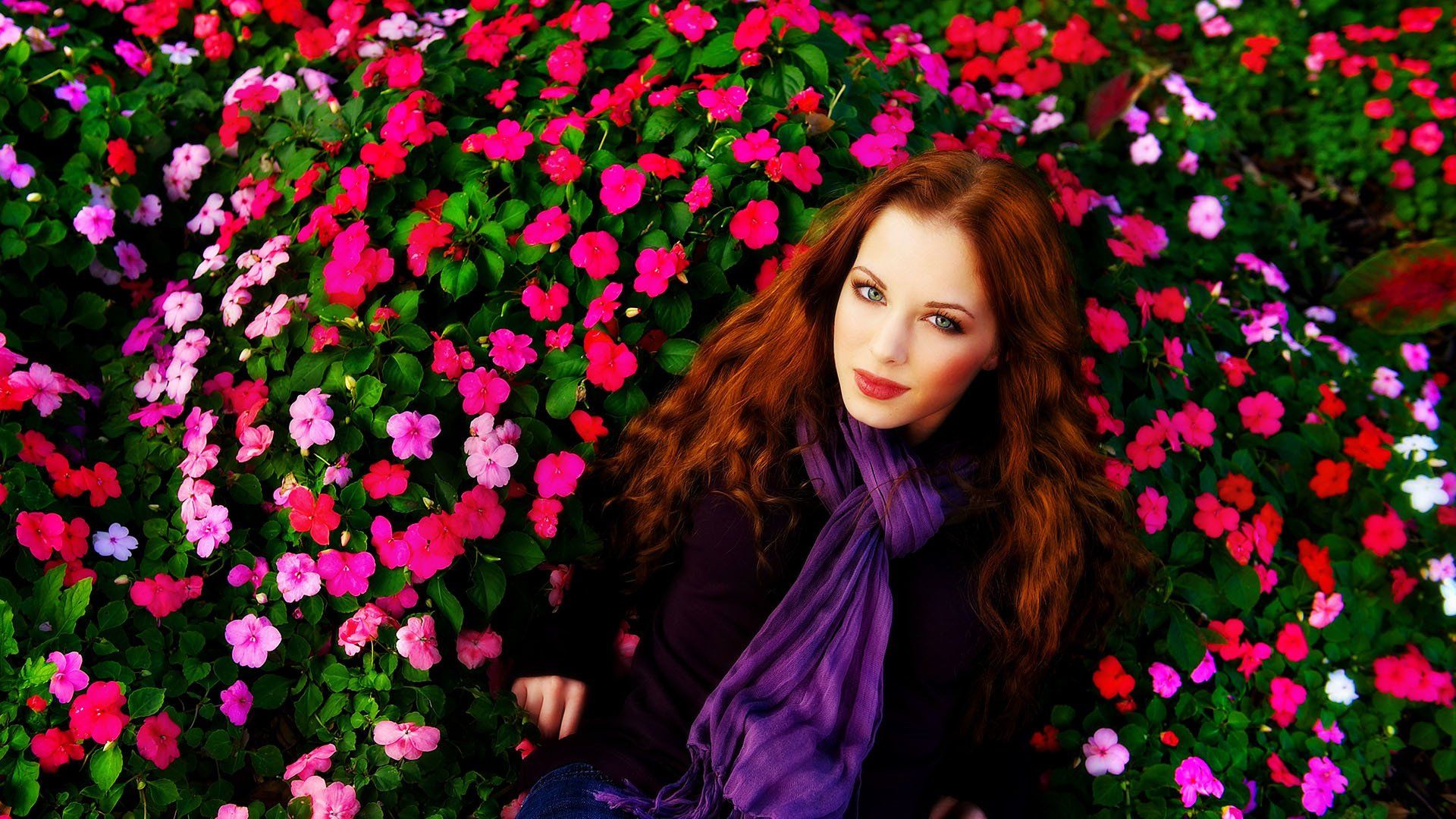 A woman in a purple scarf is sitting in a field of flowers.