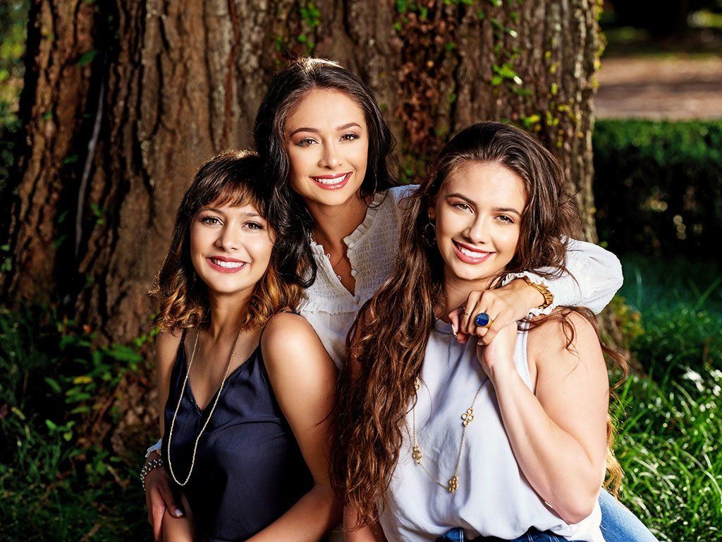 Three young women are posing for a picture under a tree.
