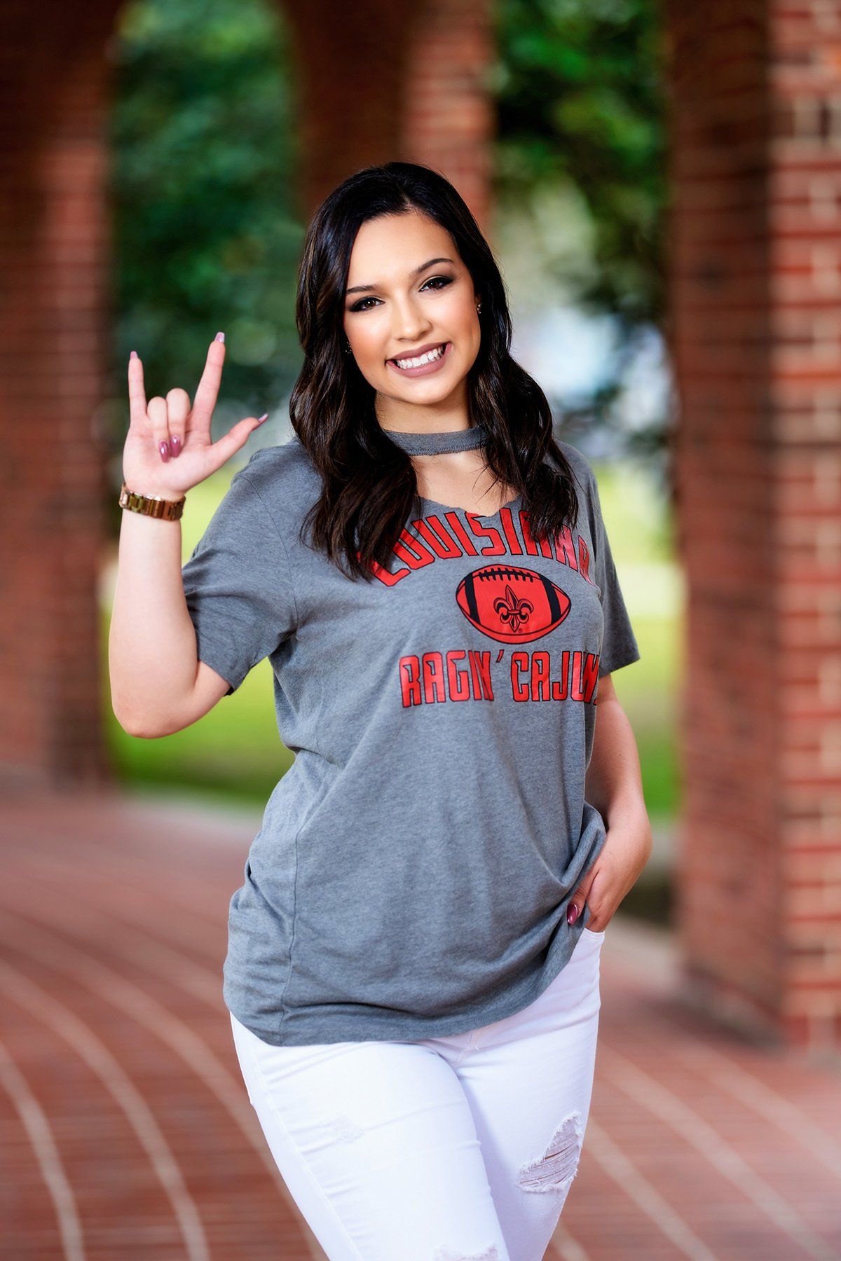 A woman wearing a gray t-shirt and white jeans is standing in front of a brick archway.