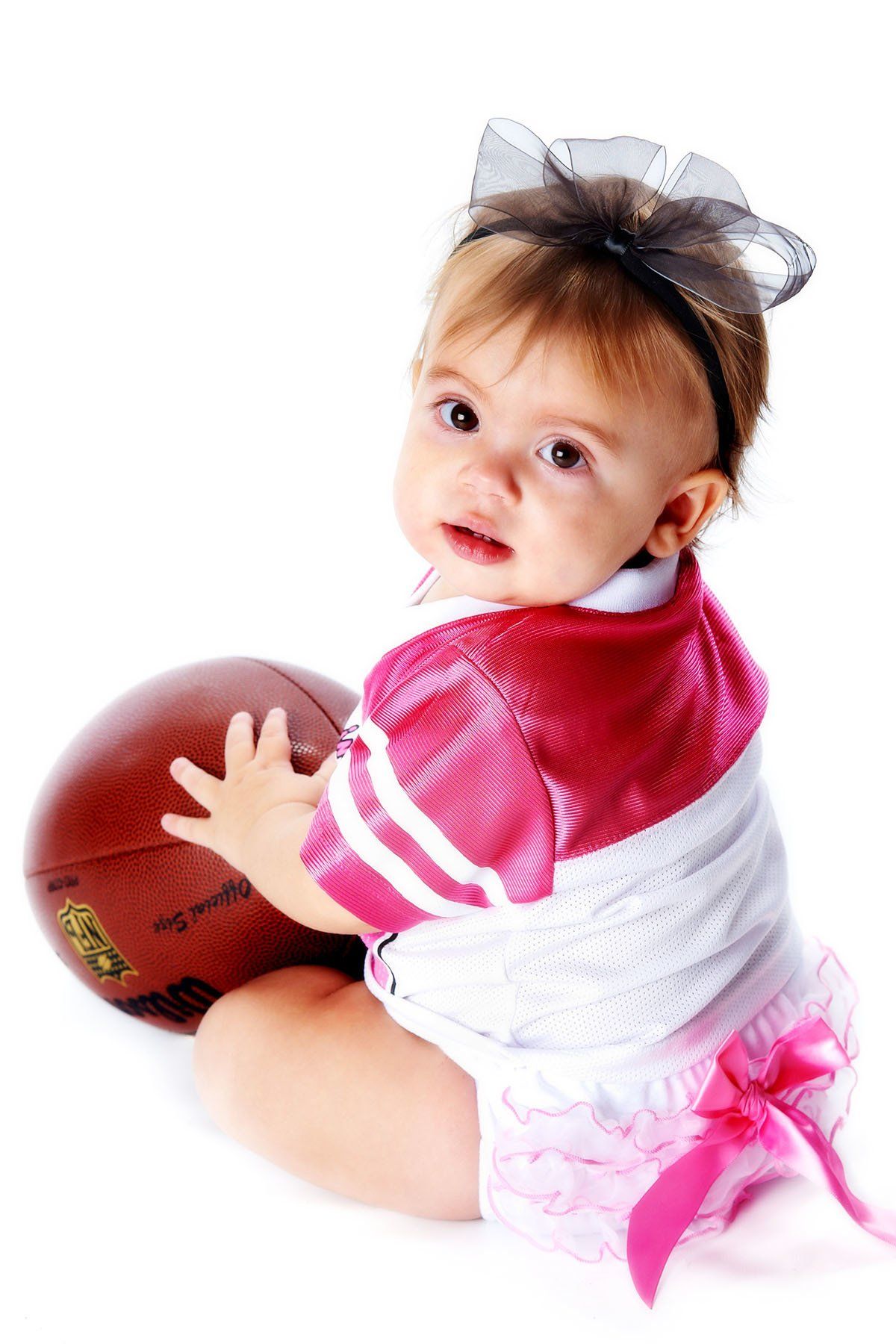 A baby in a pink and white outfit is holding a football