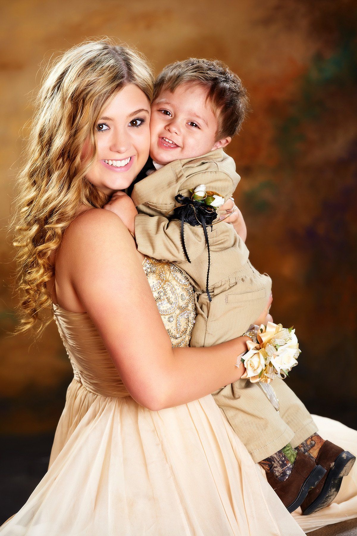 A woman in a prom dress is holding a little boy in her arms.