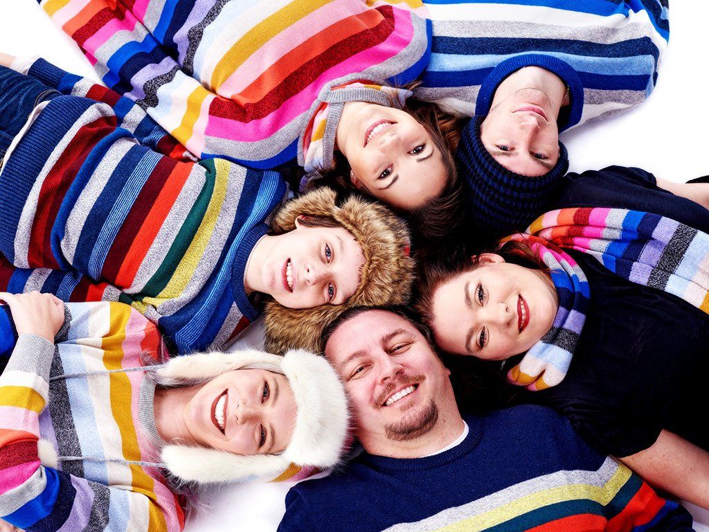A group of people wearing striped sweaters are laying in a circle on the floor.