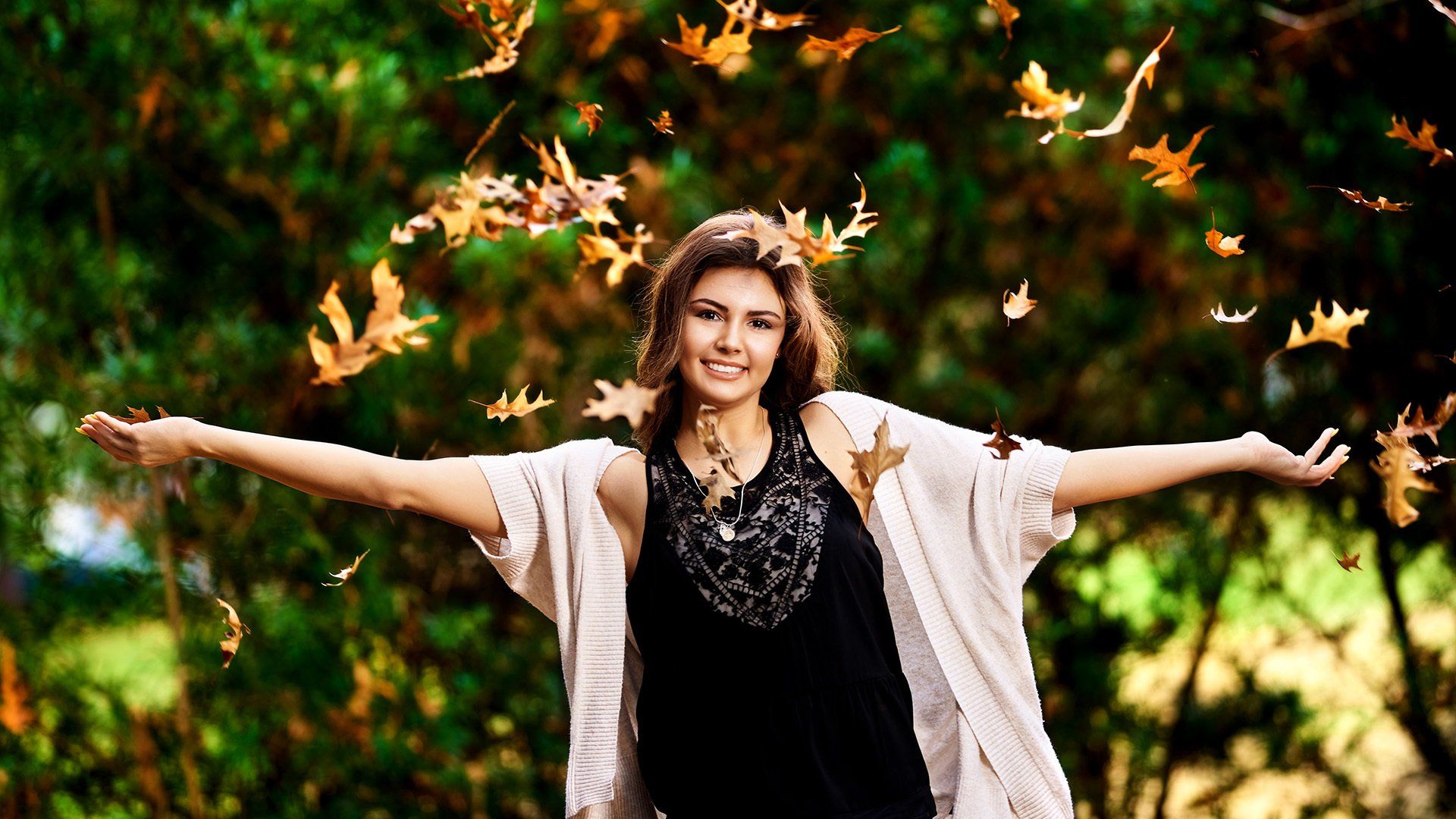 A woman is throwing leaves in the air in a park.
