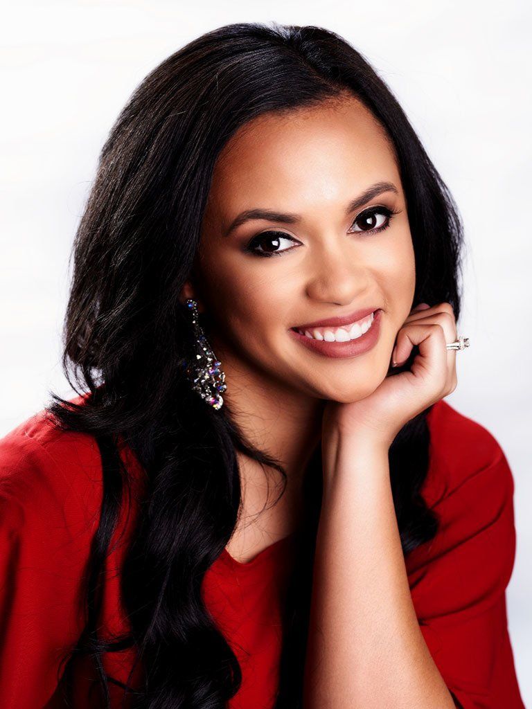A woman in a red shirt is smiling with her hand on her chin.