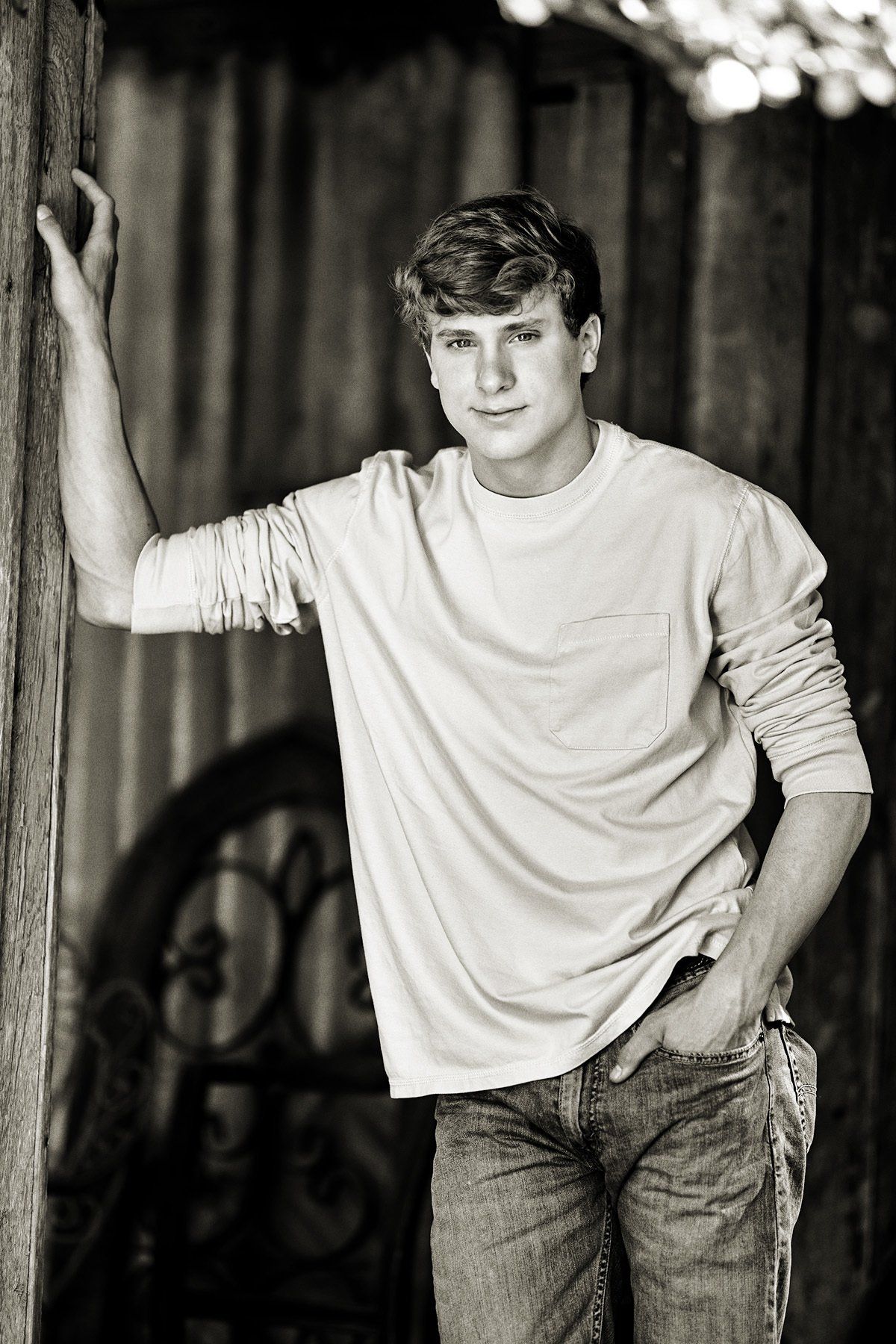 A young man leaning against a wooden wall in a black and white photo.