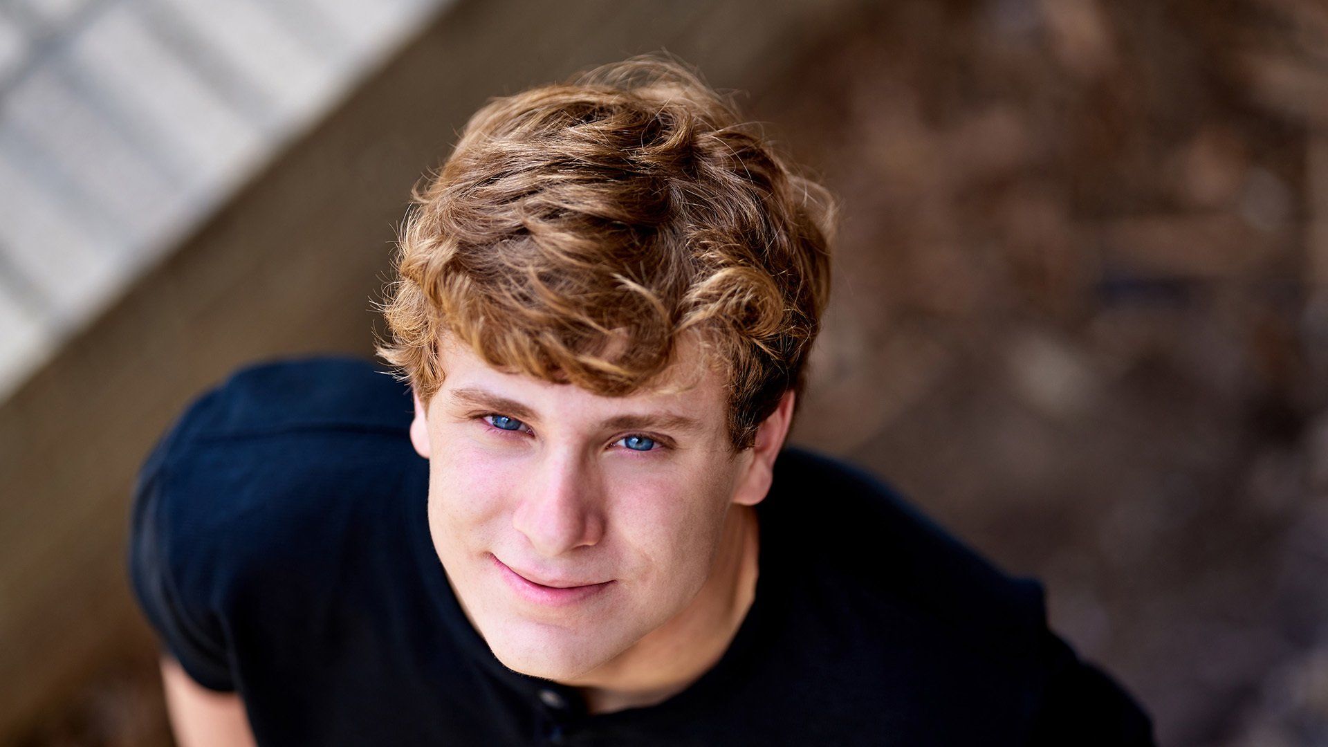 A young man in a black shirt is smiling and looking up at the camera.