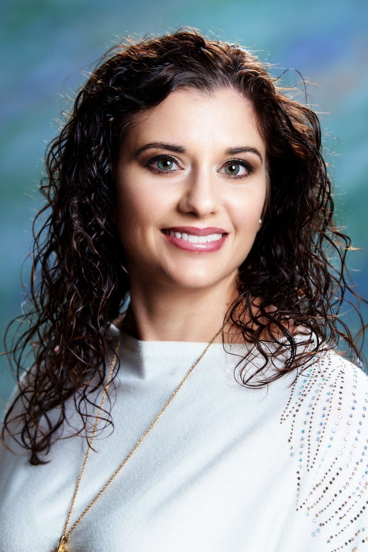 A woman with curly hair is wearing a white shirt and a gold necklace.