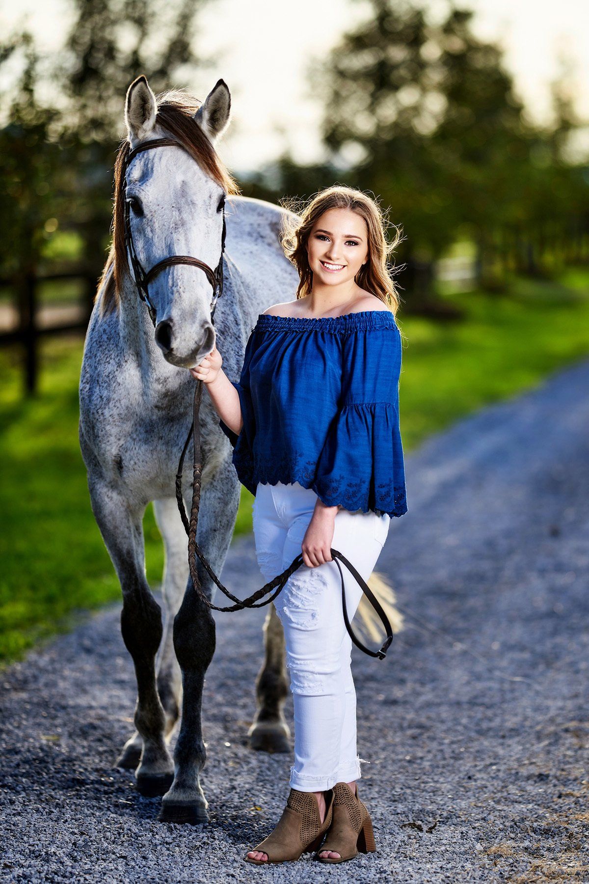 A woman is standing next to a horse on a dirt road.
