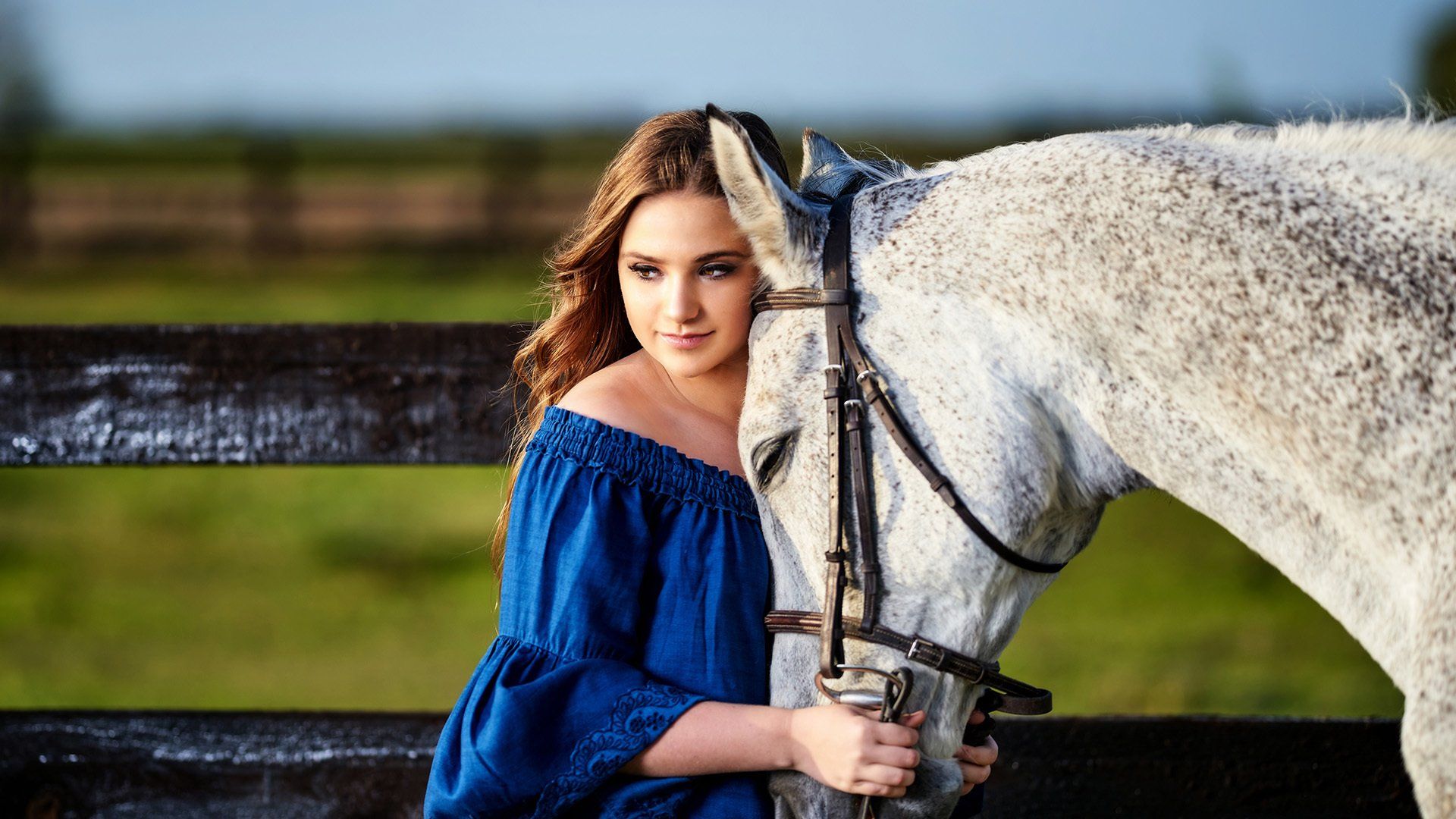 A woman in a blue dress is standing next to a white horse.