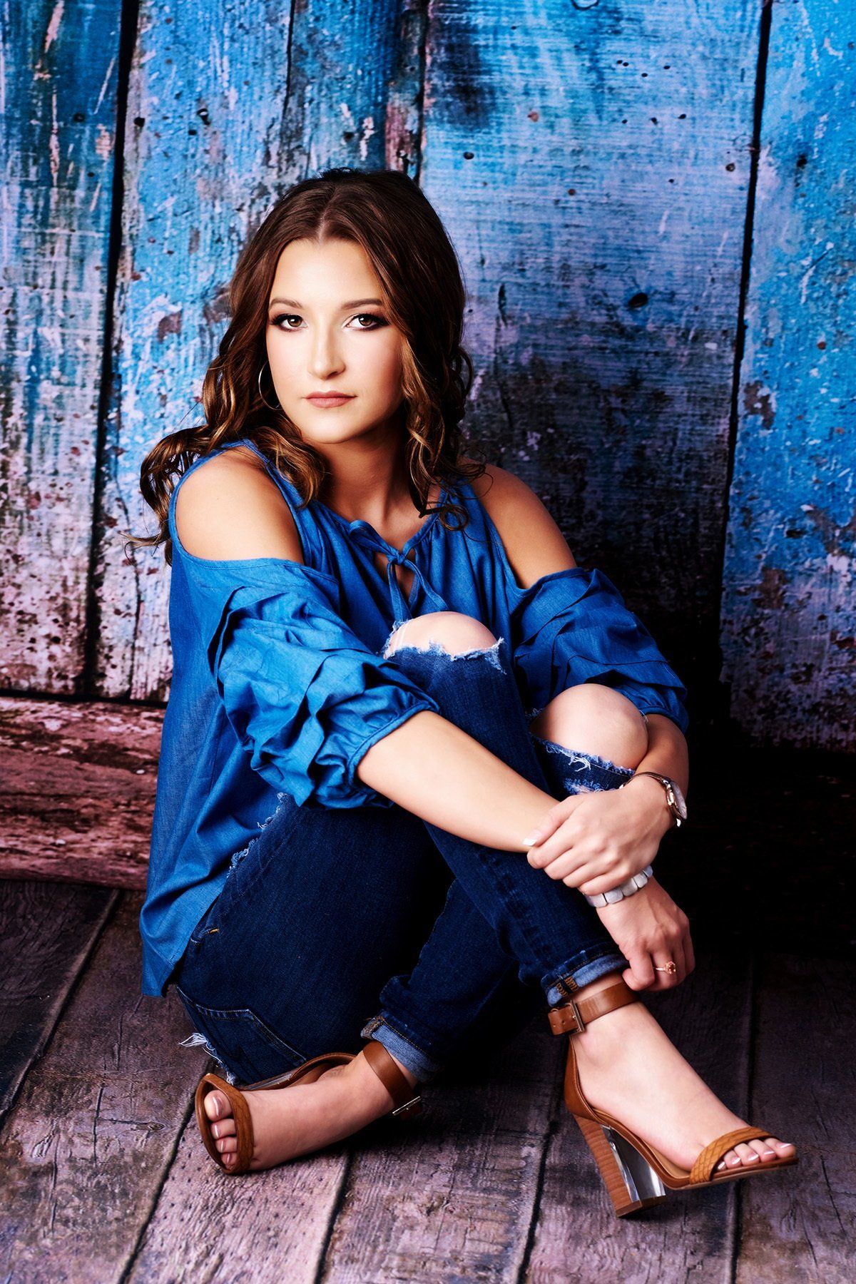 A woman in a blue shirt and jeans is sitting on the floor.