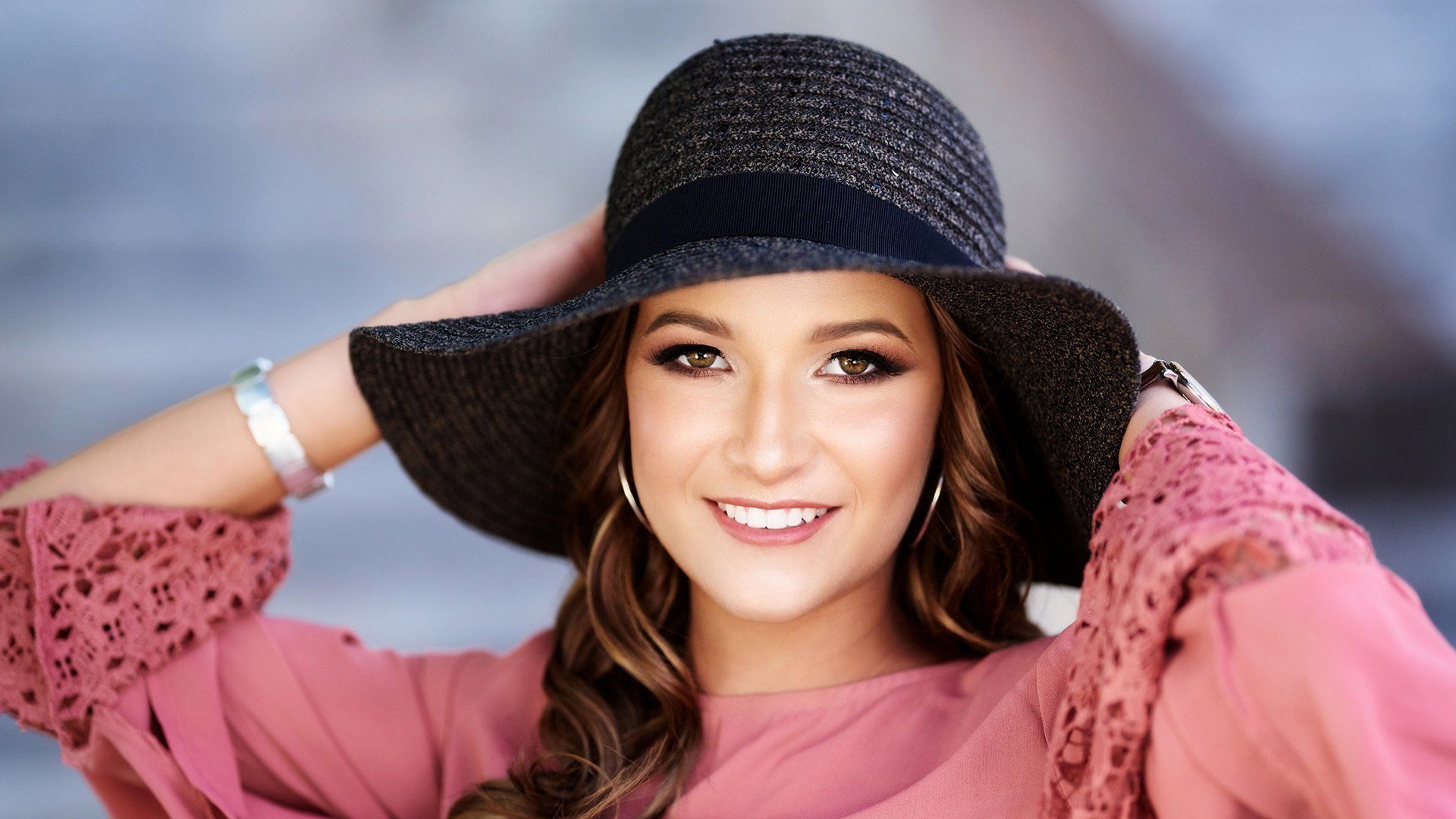 A woman wearing a hat and a pink shirt is smiling.