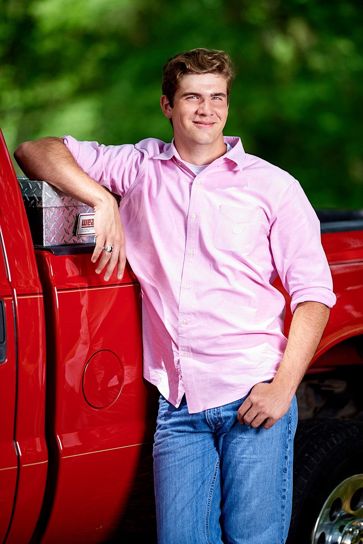 A young man in a pink shirt is leaning on a red truck.