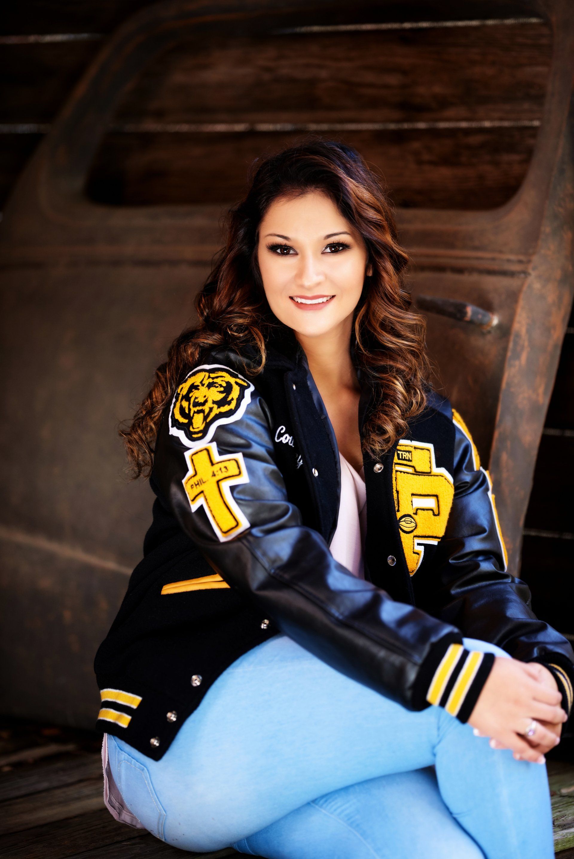A woman wearing a black and yellow letterman jacket is sitting on the ground.