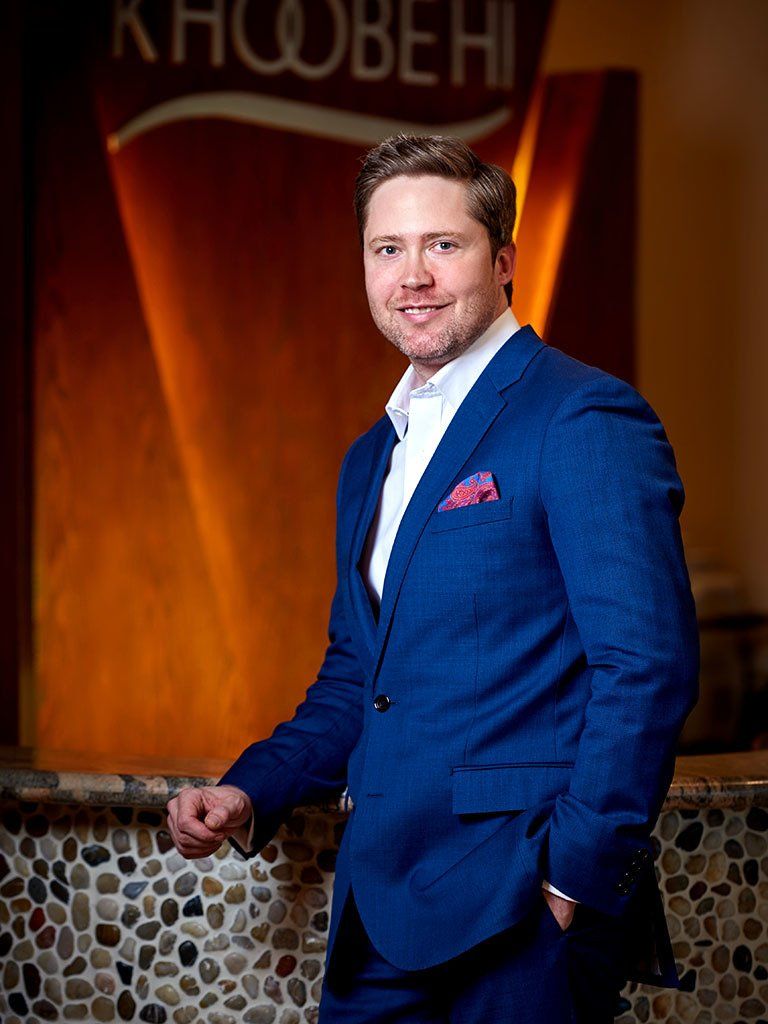 A man in a blue suit and white shirt is standing in front of a sign.